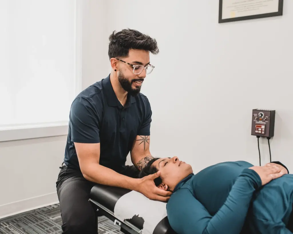 Dr. Danny Dhesa, a chiropractor, performing a neck examination on a patient in a clinic setting.