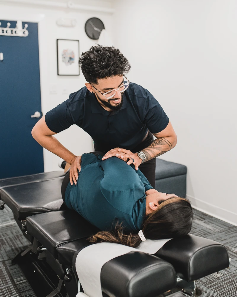 Danny Dhesa, a chiropractor, performing an adjustment on a patient lying on a treatment table.